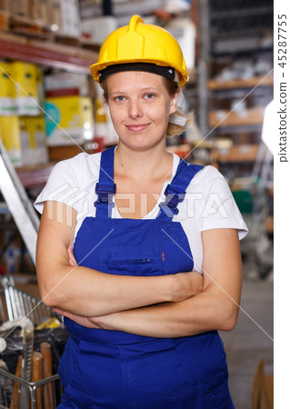 Young female in uniform and helmet standing near basket with construction materials 45287755
