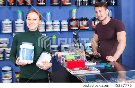 Young athletic woman satisfied with purchase of sport nutrition in store Young athletic woman satisfied with purchase of sport nutrition in store 45287776