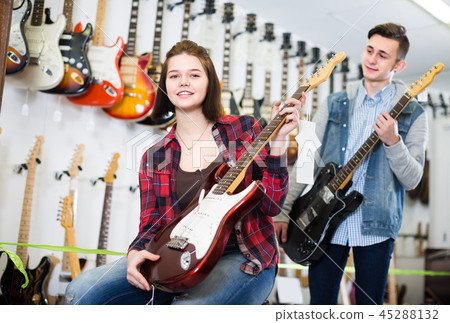 Pretty female and male teenagers customers examining electric guitars 45288132