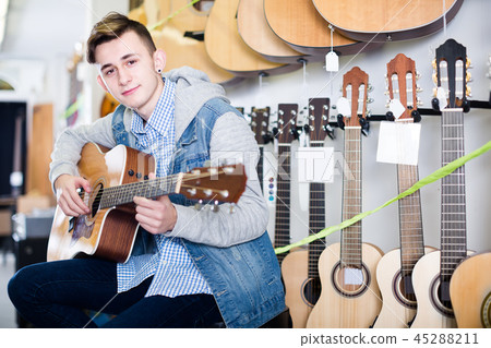 Male teenager customer deciding on acoustic guitar Male teenager customer deciding on acoustic guitar 45288211