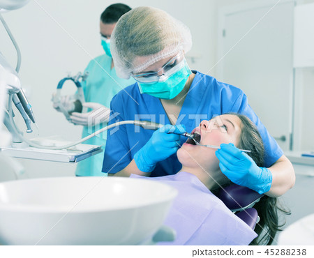 Female dentist treating girl patient with male assistant Female dentist treating girl patient with male assistant 45288238