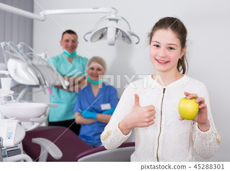 Girl with apple showing thumb up in dental clinic Girl with apple showing thumb up in dental clinic 45288301