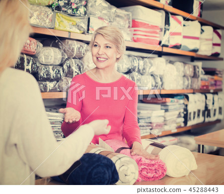 Aged female seller demonstrating coverlets to young buyer 45288443