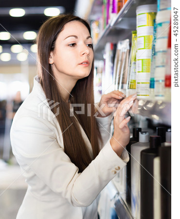 Serious young female choosing hair care products at cosmetics showroom Serious young female choosing hair care products at cosmetics showroom 45289047