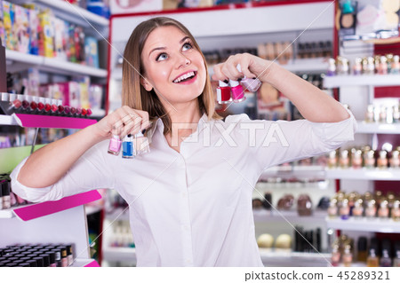 Portrait of cheerful girl with colored nail polishes in hand in store Portrait of cheerful girl with colored nail polishes in hand in store 45289321