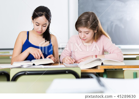 Two girls are sitting at the desk and writing homework 45289630