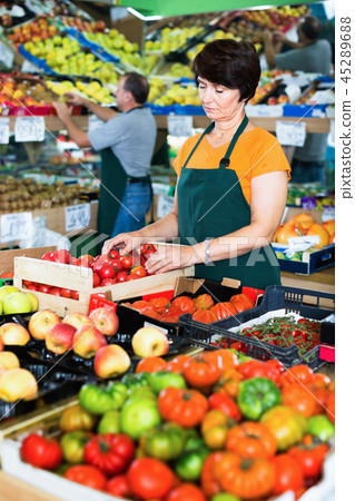 Woman seller is demonstraiting red tomatos in the store. Woman seller is demonstraiting red tomatos in the store. 45289688