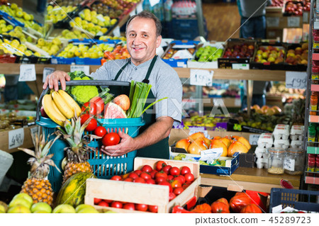 Man seller is standing with basket with fruits and vegetables Man seller is standing with basket with fruits and vegetables 45289723