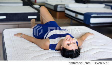 smiling customer girl is lying testing new mattress before buying it in shop smiling customer girl is lying testing new mattress before buying it in shop 45289738