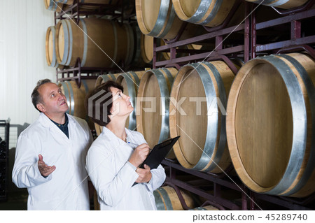 Worker of winery holds glass of red wine in hand and shows him to expert Worker of winery holds glass of red wine in hand and shows him to expert 45289740