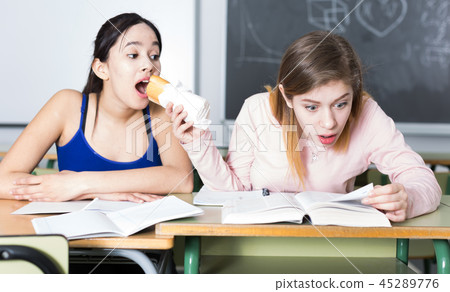 Two girls are eating sandwich at the desk and writing homework Two girls are eating sandwich at the desk and writing homework 45289776