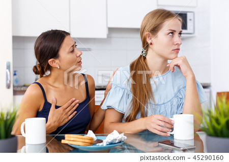 Portrait of unhappy girl friends discussion while drinking tea in home 45290160