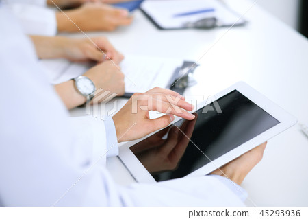 Doctor using tablet computer at medical meeting, closeup. Group of colleagues at the background Doctor using tablet computer at medical meeting, closeup. Group of colleagues at the background 45293936