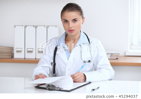 Doctor woman writing papers at the desk in hospital office. Medicine and over work concept Doctor woman writing papers at the desk in hospital office. Medicine and over work concept 45294037