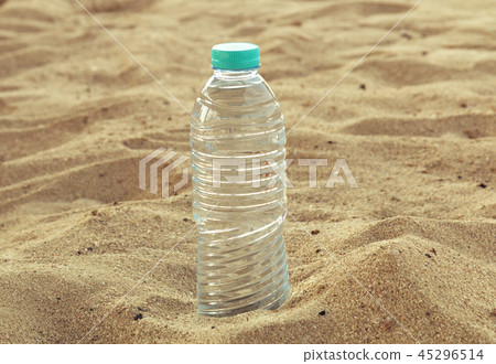 Bottle with sparkling crystal drinking water with a red lid on the sand on a background of the beach Bottle with sparkling crystal drinking water with a red lid on the sand on a background of the beach 45296514