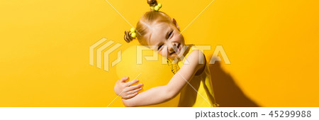 Girl with red hair on a yellow background. A girl is hugging a yellow balloon. 45299988