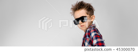 A handsome boy in a plaid shirt, gray shirt and jeans stands on a gray background. The boy in black A handsome boy in a plaid shirt, gray shirt and jeans stands on a gray background. The boy in black 45300070