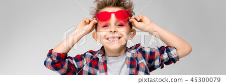 A handsome boy in a plaid shirt, gray shirt and jeans stands on a gray background. A boy in red A handsome boy in a plaid shirt, gray shirt and jeans stands on a gray background. A boy in red 45300079