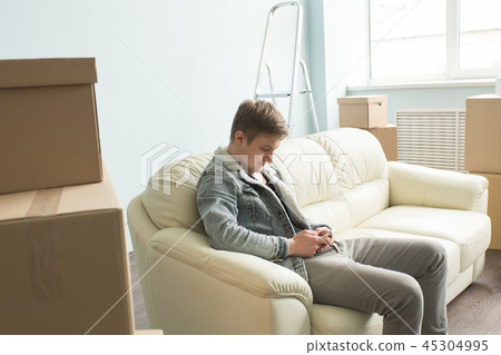 Moving process,real estate and new home concept - tired guy sits on the sofa in the empty room Moving process,real estate and new home concept - tired guy sits on the sofa in the empty room 45304995