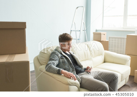 Relocation, new home and real estate concept - Cheerful young man in new home using smartphone after Relocation, new home and real estate concept - Cheerful young man in new home using smartphone after 45305010