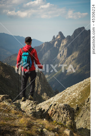 A bearded man in sunglasses and a cap with a backpack stands on top of a rock and looks into a rocky A bearded man in sunglasses and a cap with a backpack stands on top of a rock and looks into a rocky 45306214