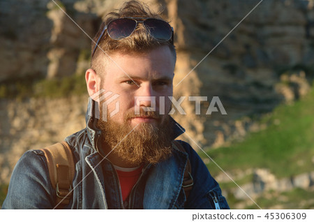 Close-up portrait of a bearded stylish traveler in a cap against epic rocks. Time to travel concept Close-up portrait of a bearded stylish traveler in a cap against epic rocks. Time to travel concept 45306309