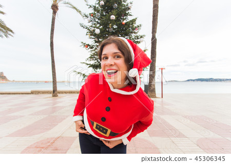 Christmas, holidays and joke concept - Funny young woman in Santa Claus costume outdoors Christmas, holidays and joke concept - Funny young woman in Santa Claus costume outdoors 45306345