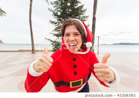 Christmas, holidays, humor and people concept- young happy woman in christmas suit at summer showing 45306365