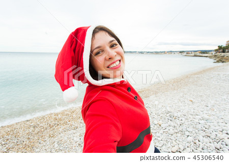 Christmas, humor and people concept - young woman in Santa suit making selfie near the sea at summer 45306540