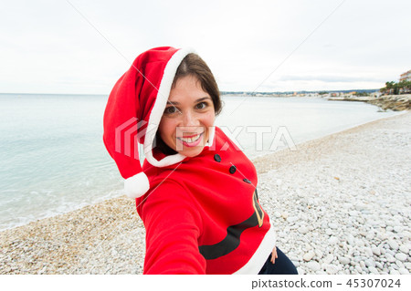 Christmas, humor and people concept - young woman in Santa suit making selfie near the sea at summer Christmas, humor and people concept - young woman in Santa suit making selfie near the sea at summer 45307024