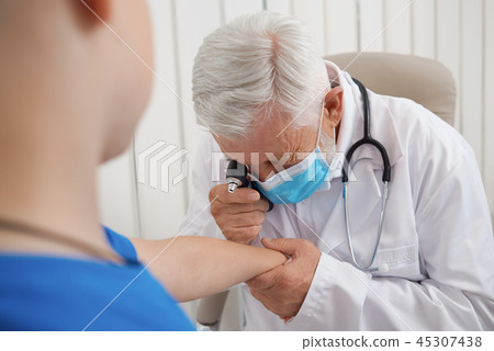 Doctor using tool for examining hand of patient. Doctor using tool for examining hand of patient. 45307438