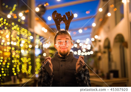 Christmas and holiday concept - Happy man in Christmas deer costume with sparkler 45307920