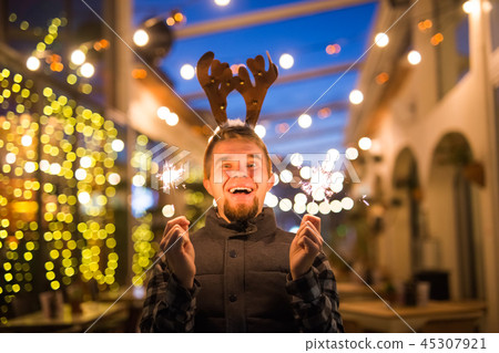 People, holidays and Christmas concept - young funny man in christmas deer costume with bengals People, holidays and Christmas concept - young funny man in christmas deer costume with bengals 45307921