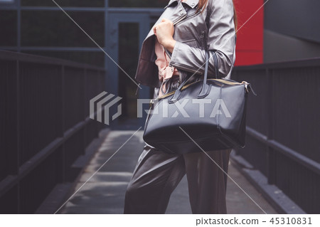 Trendy woman in silver pants jacket with black bag in hand street look. Fashionable outfit Trendy woman in silver pants jacket with black bag in hand street look. Fashionable outfit 45310831