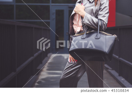 Trendy woman in silver pants jacket with black bag in hand street look. Fashionable outfit Trendy woman in silver pants jacket with black bag in hand street look. Fashionable outfit 45310834