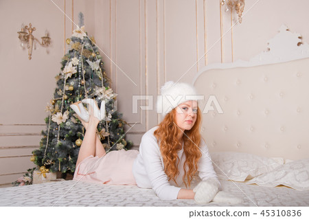 Happy woman with an ornament sitting beside a Christmas tree in the room 45310836