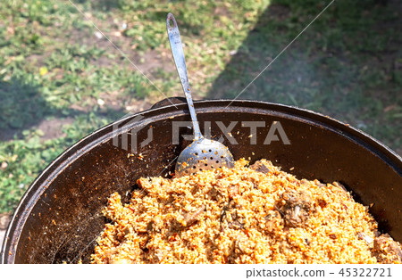 Cooking traditional Uzbek pilaf in a cauldron 45322721