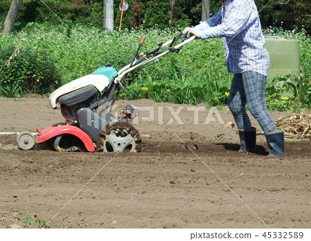 A person cultivating the field with a small cultivator 45332589