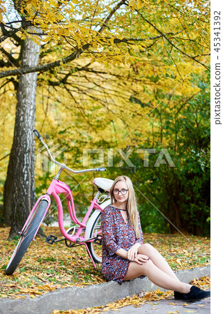 Blond fashionable long-haired attractive girl in short dress with lady bicycle in sunny park. Blond fashionable long-haired attractive girl in short dress with lady bicycle in sunny park. 45341392
