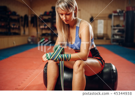 Female kickboxer sitting on punching bag in gym Female kickboxer sitting on punching bag in gym 45344938