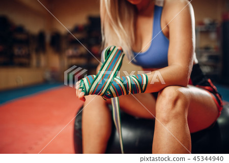 Female kickboxer sitting on punching bag in gym Female kickboxer sitting on punching bag in gym 45344940