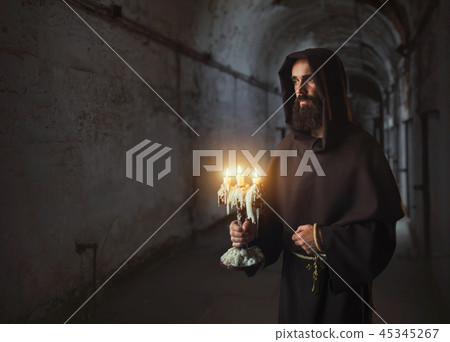 Medieval monk in robe holds a candlestick in hands 45345267