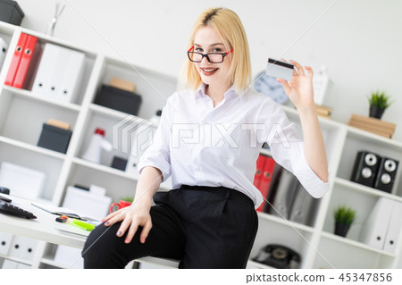 A young girl leaned on the Desk in the office and holding a Bank card. A young girl leaned on the Desk in the office and holding a Bank card. 45347856