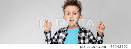 A handsome boy in a plaid shirt, blue shirt and jeans stands on a gray background. The boy clamped A handsome boy in a plaid shirt, blue shirt and jeans stands on a gray background. The boy clamped 45348302