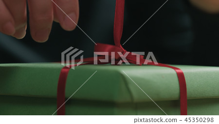 Macro shot of female hands tying red ribbon bow on green paper gift box 45350298