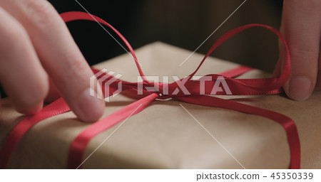 closeup shot of young female hands unties red ribbon bow on craft paper gift box closeup shot of young female hands unties red ribbon bow on craft paper gift box 45350339