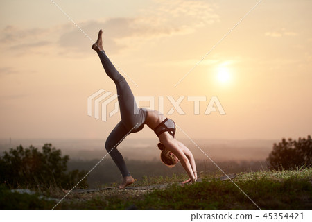Attractive slim young woman doing yoga exercises outdoors on copy space background of beautiful sky. Attractive slim young woman doing yoga exercises outdoors on copy space background of beautiful sky. 45354421