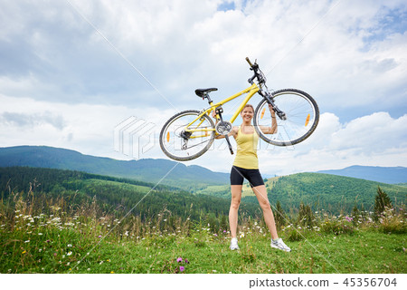 Attractive female cyclist with yellow mountain bicycle, enjoying sunny day in the mountains 45356704