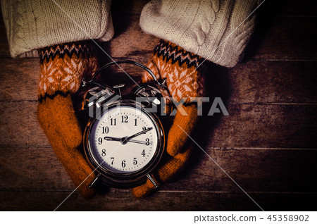 hands in mittens holding an alarm clock with bell 45358902