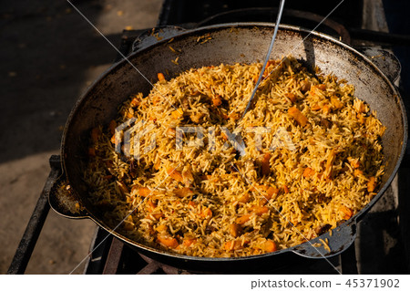 Tasty Uzbek pilaf in cauldron on fire in open air  45371902